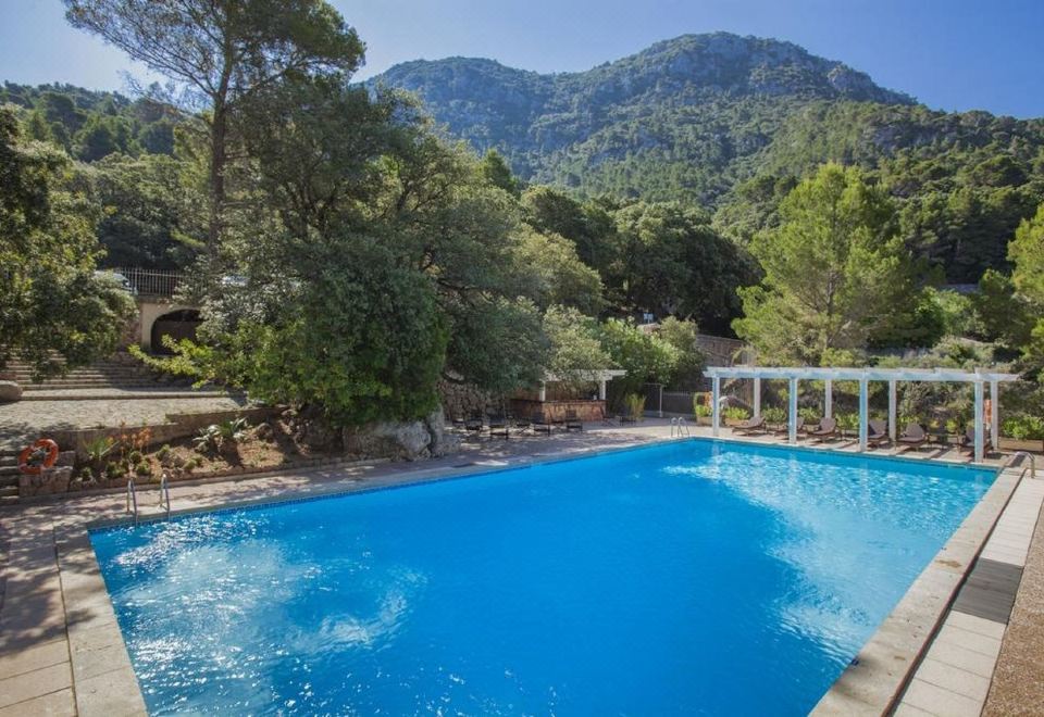 a large outdoor swimming pool surrounded by trees and mountains , with lounge chairs and umbrellas placed around the pool area at Bordoy Continental Valldemossa