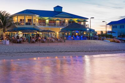 a beach resort with a restaurant and dining area on the sand , illuminated by colorful lights at Wyndham Reef Resort Grand Cayman