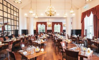 a large dining room with many tables and chairs , a chandelier hanging from the ceiling , and a red door at the end of the room at Low Wood Bay