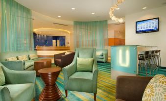 a modern living room with blue and green furniture , a reception desk , and a large screen at SpringHill Suites Alexandria