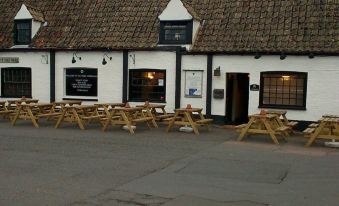 an empty outdoor seating area with several wooden benches and tables , located outside a white building at Three Horseshoes Inn