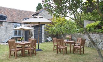 a patio area with wooden tables and chairs , surrounded by greenery and an umbrella at The White Hart