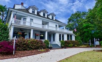 a large white house with a stone walkway leading to the front door , surrounded by trees at Magnolia Inn