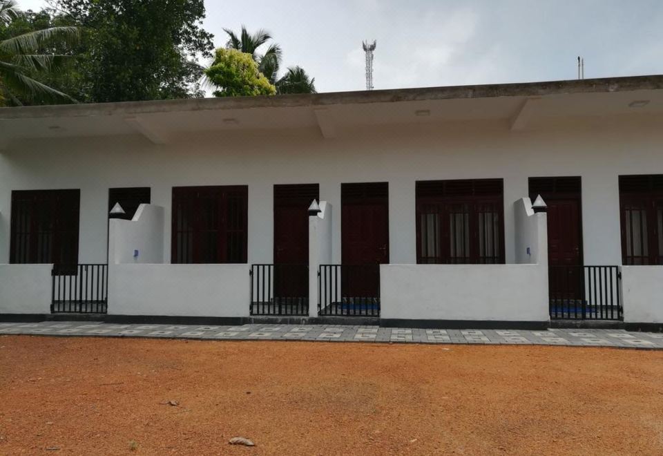 a white house with four windows and a porch is surrounded by red gravel and trees at Sea Breeze