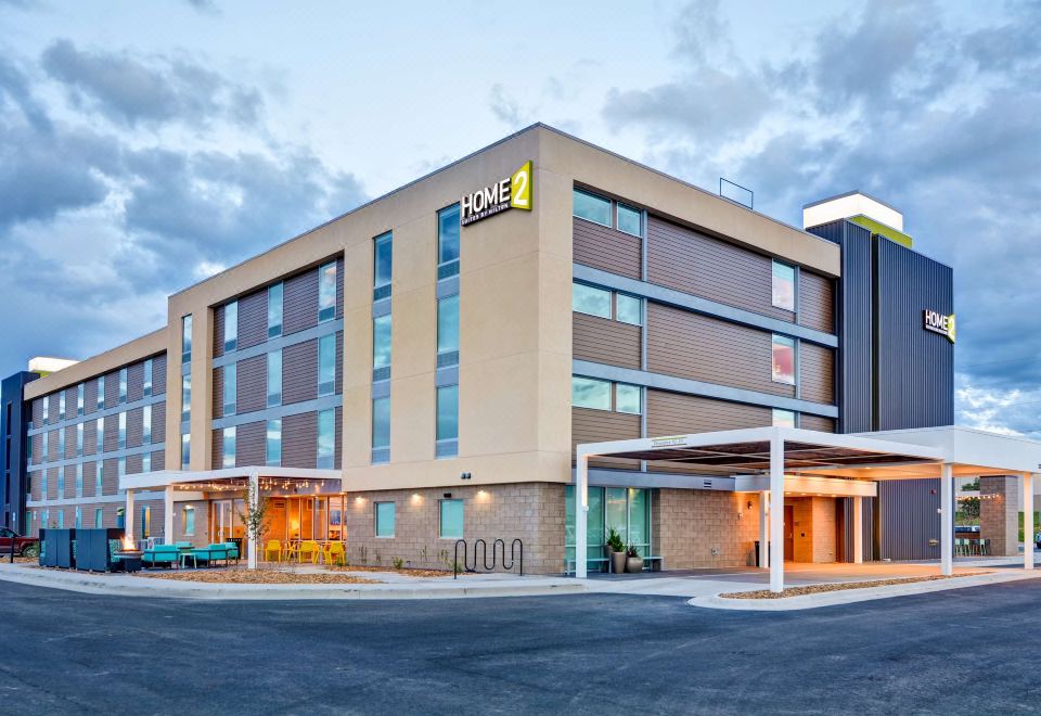 "a modern hotel building with the name "" home 2 "" displayed on its side , surrounded by other buildings and cars" at Home2 Suites by Hilton Helena