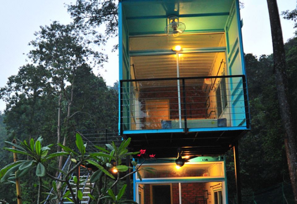 a blue container house built on stilts in the middle of a forest , with a staircase leading up to it at Sarang by the Brook