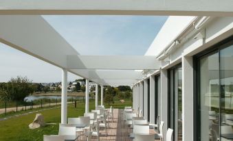 a modern outdoor dining area with white tables and chairs , surrounded by greenery and a view of the surrounding area at Best Western Plus Hotel les Rives du Ter