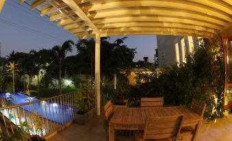 a wooden patio with a table and chairs , surrounded by greenery and lit up at night at Capital Villa