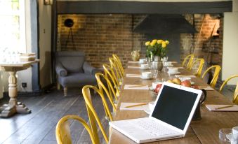a long wooden table with yellow chairs and a laptop on it , surrounded by a brick wall and some plants at The Crown