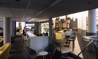 a modern , well - lit restaurant with a bar and seating area , featuring white chairs and blue tables at Novotel Chateau de Versailles