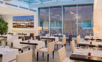 a modern restaurant with multiple dining tables , chairs , and a large screen tv mounted on the wall at NH Orio Al Serio