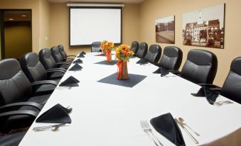 a conference room with a long table , black chairs , and a projector screen , decorated with flowers at Holiday Inn Port Arthur - Park Central by IHG