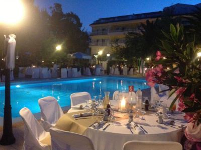 a table is set with wine glasses , candles , and silverware near a pool at night at Hotel Summery