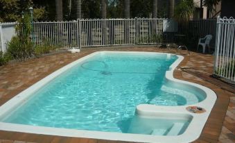 a large swimming pool with a white border and a stone step is surrounded by a patio and chairs at Bridge Motel