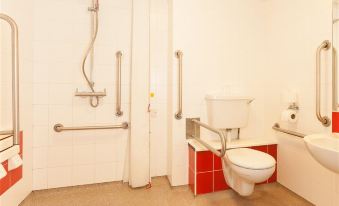 a bathroom with a toilet , sink , and shower , as well as various items such as a handrail and mirror at Travelodge Wincanton