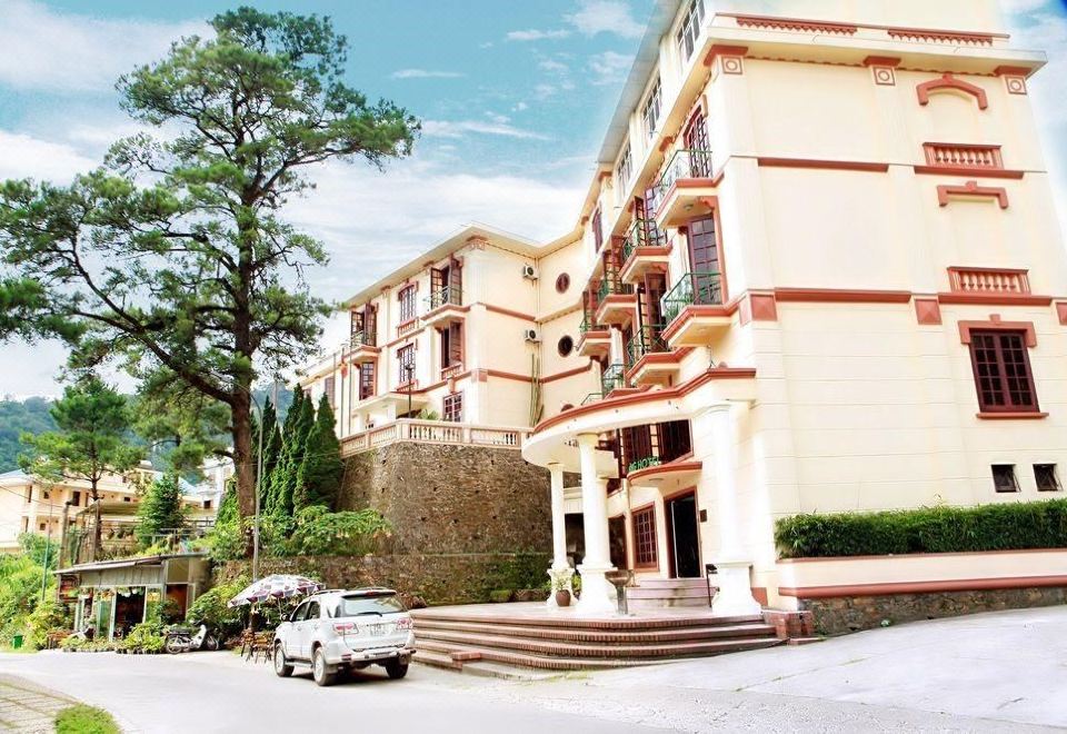 a white car is parked in front of a building with stairs and trees surrounding it at Cay Thong Hotel