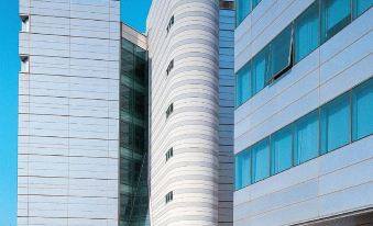 a modern building with a curved design and blue glass windows is shown against a clear sky at B&B Hotel Trapani Crystal