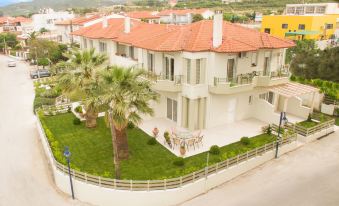 a large white house with a red roof , surrounded by trees and a fence , on a sunny day at Minthi Boutique Apartments