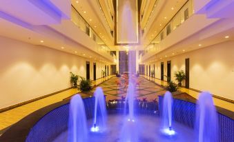 a large indoor fountain with multiple water jets shooting up in the air , surrounded by white walls and a ceiling filled with lights at Sarovar Portico, Somnath