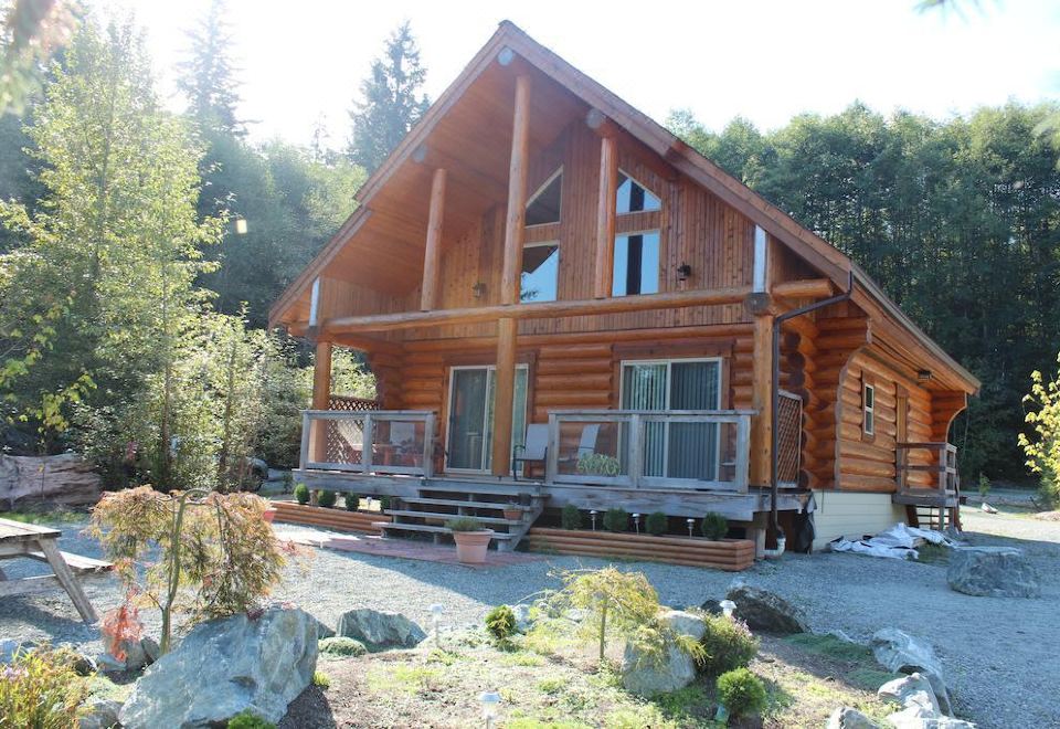 a large log cabin surrounded by trees and grass , with a deck extending from the front of the building at Beaver Lake Resort