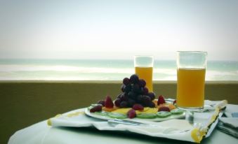 a table with a plate of fruit and two glasses of orange juice , set against the backdrop of a beautiful ocean view at Arribas Sintra Hotel