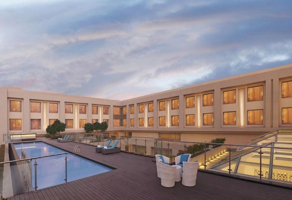 a large , modern building with a swimming pool and lounge chairs is shown at sunset at DoubleTree by Hilton Agra