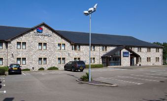 a hotel with a stone facade and large windows is shown in the daytime , with a car parked in front at Travelodge Kendal