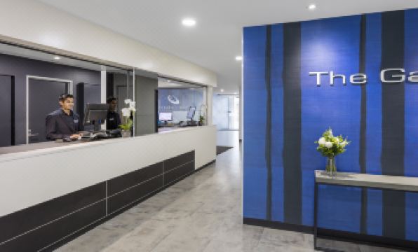 "a modern office interior with a reception area , two people working behind the counter , and a blue wall with the word "" theta "" written in" at IStay Precinct Adelaide