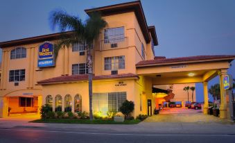 a large yellow hotel building with a blue sign and palm trees in front of it at Best Western Oceanfront