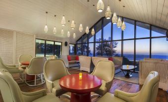 a modern lounge area with a large window offering a view of the ocean , red tables , and white chairs at W Goa