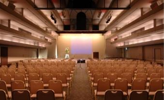 an empty conference room with rows of brown chairs and a large screen at the front at HOTEL MYSTAYS Utsunomiya