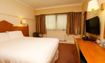 a large bed with white sheets is in a room with brown curtains and a desk at Fairways Lodge & Leisure Club