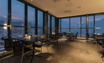 a restaurant with large windows overlooking a cityscape , where people are enjoying their meals and drinks at Scandic Narvik