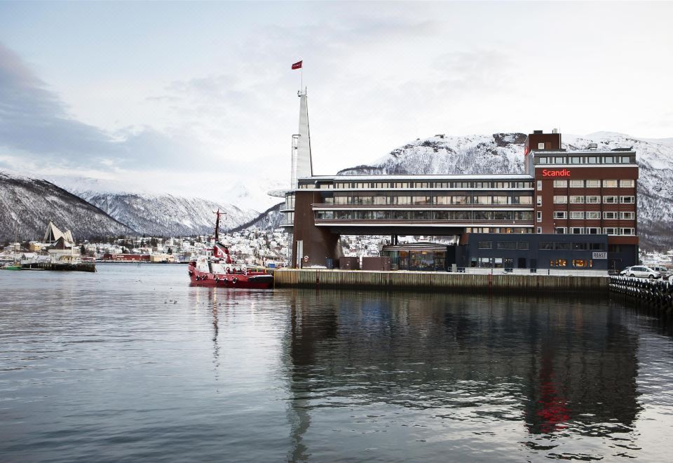 a large red and white ship is docked at a pier , surrounded by snow - covered mountains in the background at Scandic Ishavshotel