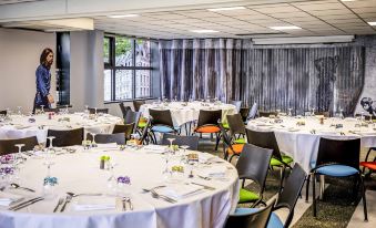 a well - decorated dining room with several round tables covered in white tablecloths , ready for a formal event at Ibis Styles Lille Marcq-en-Baroeul