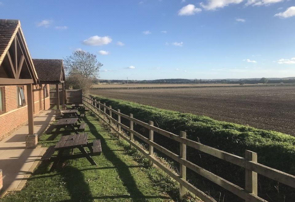 a wooden fence with a table and chairs on the side , overlooking a field and water at The Carrington Arms