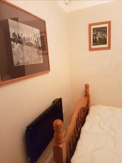 a small room with a wooden bed , a tv mounted on the wall , and a framed picture hanging above the bed at Knights