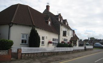 a white house with a red - tiled roof and brown - tiled walls is surrounded by greenery , situated on a street at Malt House