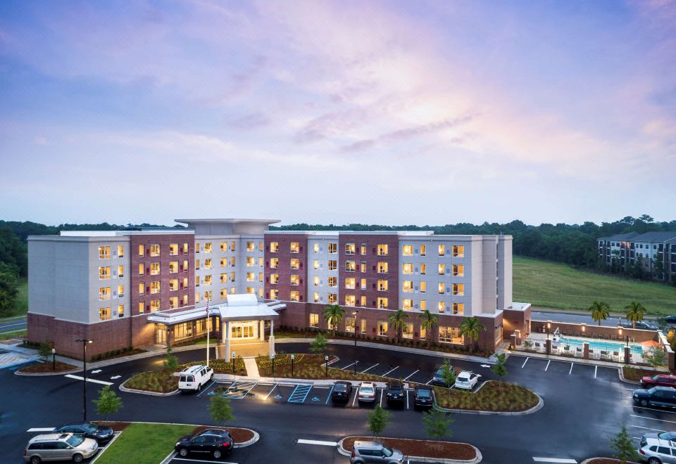 a large hotel with a parking lot in front of it and the sun setting behind it at Hyatt House Charleston/Mount Pleasant