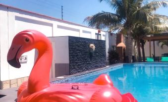 a large red flamingo floatie is floating in a pool , surrounded by palm trees and buildings at Costa Esmeralda
