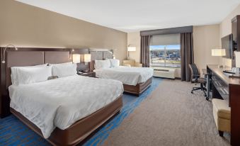 a hotel room with two beds , a window , and a chair , all set against the backdrop of a cityscape at Holiday Inn Owensboro Riverfront