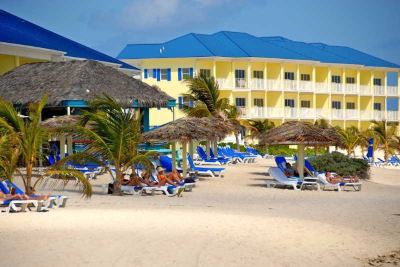 a tropical resort with yellow buildings , blue umbrellas , and white sandy beach , under a clear blue sky at Wyndham Reef Resort Grand Cayman