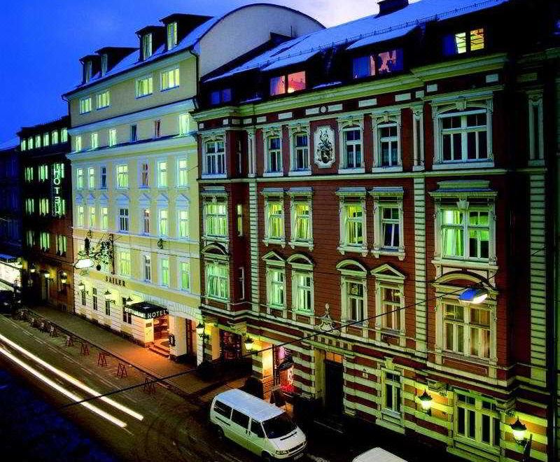 a city street at night , with a tall building in the background and several cars parked on the street at Hotel Sailer