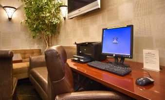 a computer desk with a monitor , keyboard , and mouse is set up in a room with a couch and television at Best Western the Inn at Ramsey