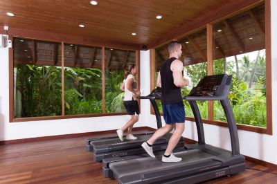 two people are working out on treadmills in a gym with large windows and tropical plants outside at Vilamendhoo Island Resort & Spa