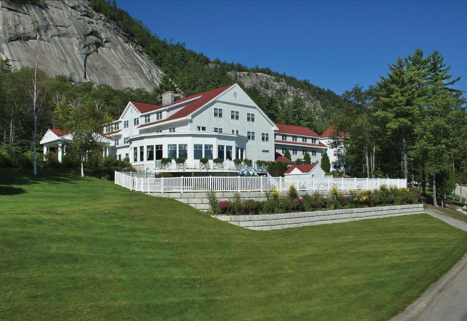 a large white house with a red roof is surrounded by green grass and trees at White Mountain Hotel and Resort