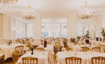 a large dining room with many tables and chairs , all covered in white tablecloths , under a chandelier at Hotel Metropole