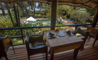 a dining table set with plates and utensils , situated on a balcony overlooking a pool and lush greenery at Maravu Taveuni Lodge