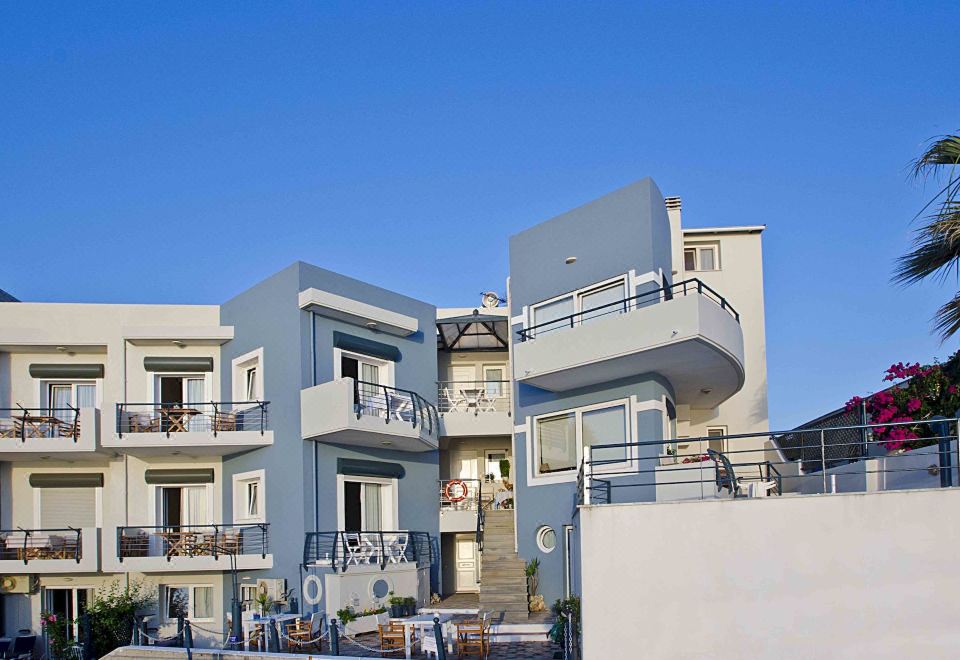 a blue apartment building with balconies and stairs , surrounded by a fence and trees , under a clear blue sky at Sea Breeze