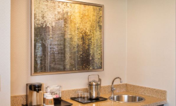 a kitchen counter with a sink , coffee maker , and two stainless steel containers next to a painting at Sheraton Suites Chicago Elk Grove